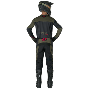 Eine Person in einem dunkelgrünen und schwarzen O'NEAL-Motocross-Outfit, komplett mit Helm, Handschuhen und Stiefeln, trägt O'NEAL ELEMENT Pants RACEWEAR und steht mit den Händen in den Hüften von der Kamera weg.