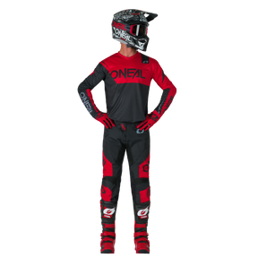 Eine Person in schwarz-roter Motocross-Kleidung mit Helm, Schutzbrille, Handschuhen und Stiefeln trägt O'NEAL ELEMENT Pants RACEWEAR und steht mit den Händen auf den Hüften, leicht zur Seite gewandt. Der Markenname O'NEAL ist auf dem Outfit sichtbar.