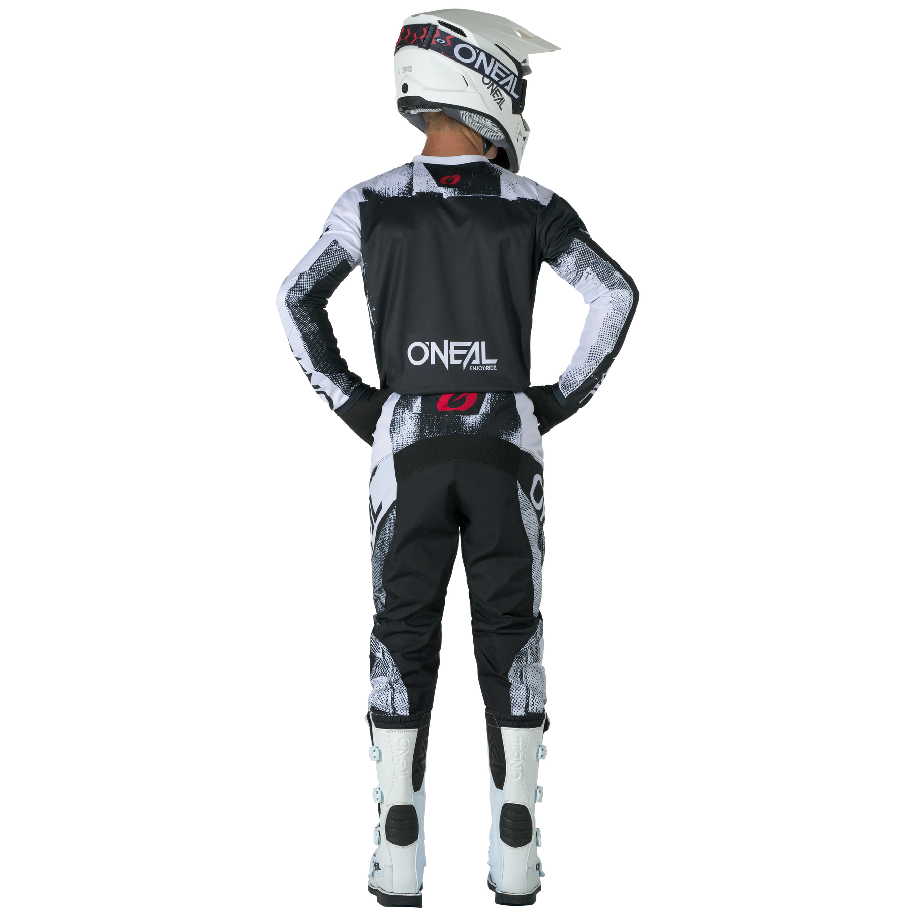 Ein Fahrer in schwarzer, weißer und grauer Kleidung steht mit den Händen in den Hüften und dem Blick nach vorne gerichtet. Er trägt einen O'NEAL-Vollhelm, Stiefel und den O'NEAL ELEMENT Pants ROLLER mit roten Logo-Akzenten vor einem schwarzen Hintergrund.