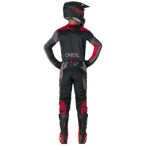 Eine Person in schwarzer und roter O'NEAL ELEMENT Pants ROLLER Motocross-Ausrüstung, Helm und Stiefeln steht mit den Händen in den Hüften von der Kamera abgewandt. Auf der Rückseite des Outfits ist das "O'NEAL"-Logo zu sehen.