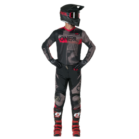 Eine Person in voller Motocross-Ausrüstung - schwarzes und rotes O'NEAL-Trikot, Handschuhe, rote Stiefel und O'NEAL ELEMENT Pants ROLLER - steht da und schaut zur Seite.