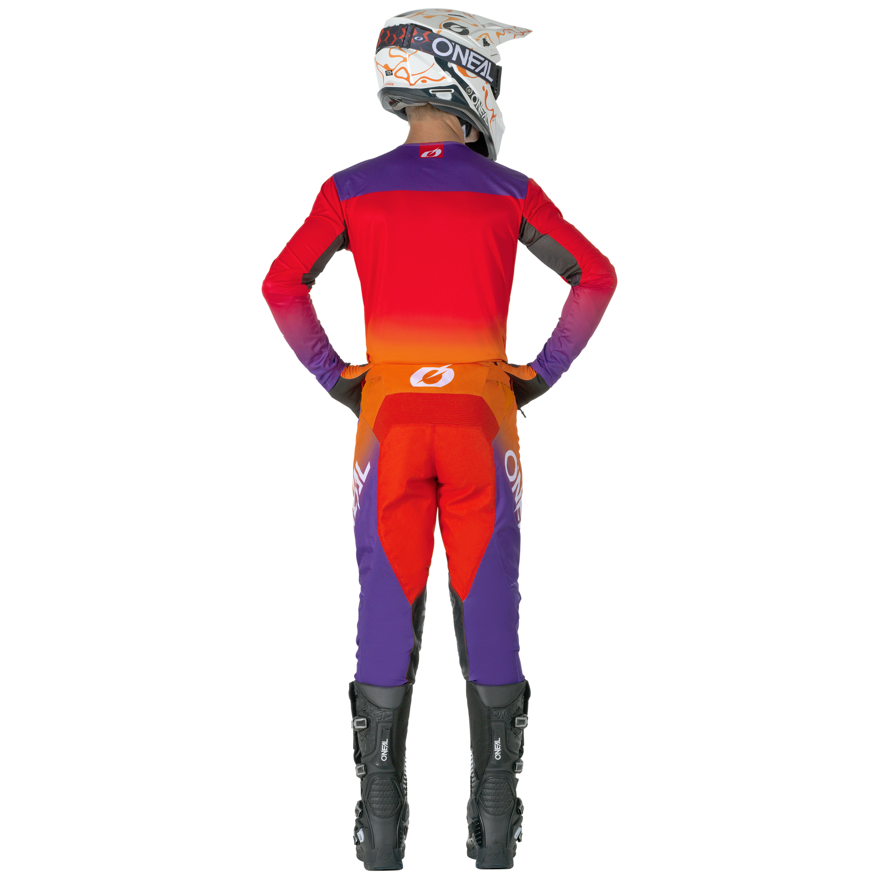 Eine Person in einem roten, orangefarbenen und lilafarbenen O'NEAL MAYHEM Hose HEXX-Motocross-Anzug mit schwarzen Stiefeln und einem weißen Helm steht mit den Händen in den Hüften. Das Outfit weist O'NEAL-Branding auf dem Helm, dem Rücken und den Beinen auf.