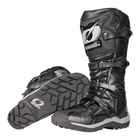 Der O'NEAL RMX Adventure Boot in Schwarz und Grau verfügt über robuste Sohlen, Schutzschnallen und verstärkte Schienbeinschützer. Ein Stiefel steht aufrecht, während der andere seitlich liegt, um das Profil zu betonen - ideal für Motorsportler.