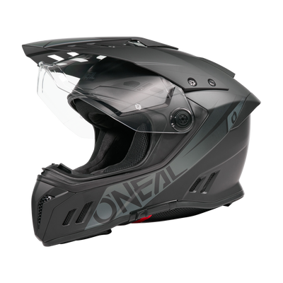 Ein Schwarz/Weiß O'NEAL SIERRA RS Helm SOLID mit klarem Visier, aerodynamischen Belüftungsöffnungen, Quin Smart Safety Sensor und fetten seitlichen Schriftzügen wird vor einem schlichten schwarzen Hintergrund dargestellt.