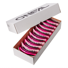 Öffne die weiße Box mit der O'NEAL B-ZERO Goggle (10 Stück). Darin findest du pink/klare Schutzbrillen, ordentlich angeordnet und durch Schutzmaterial getrennt. Der Deckel ist teilweise geöffnet und zeigt stolz das O'NEAL-Logo.