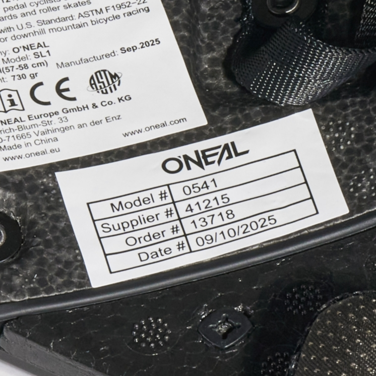 Nahaufnahme eines weißen Etiketts auf einem schwarzen O'NEAL-Produkt mit der Modellnummer 0541, der Lieferantennummer 41215, der Bestellnummer 13718 und dem Datum 09/10/2025.