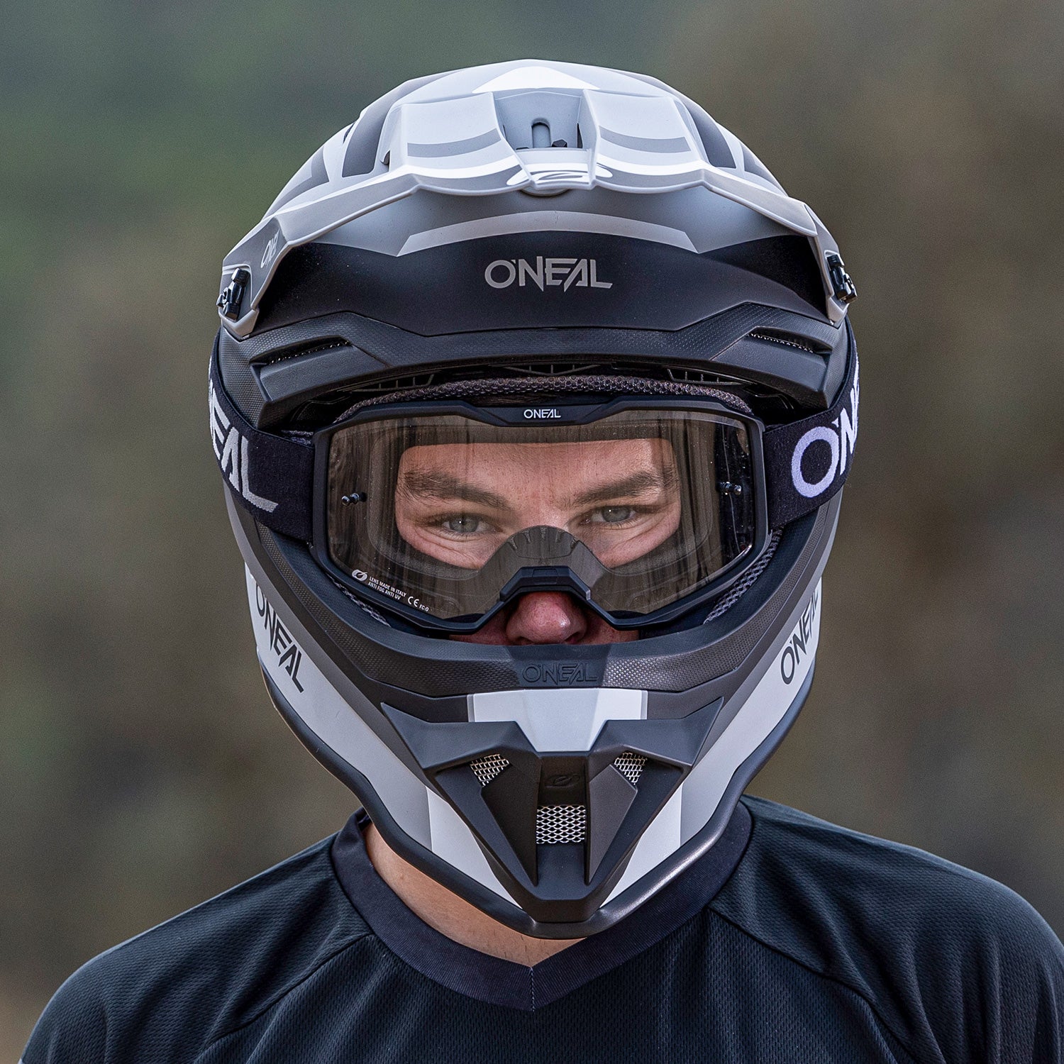 Eine Person trägt einen schwarz-weißen O'Neal-Motocross-Integralhelm mit Schutzbrille. Der Hintergrund ist leicht verschwommen, sodass die Aufmerksamkeit auf die Schutzausrüstung der Person gerichtet ist.