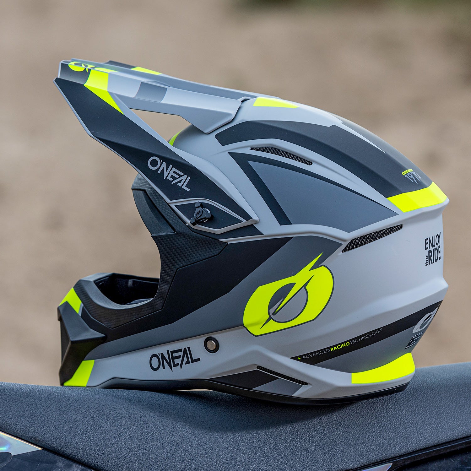 Nahaufnahme eines sportlichen Motocrosshelms mit schlankem Design. Der Helm ist hauptsächlich grau und schwarz mit neongelben Akzenten. Er verfügt über ein langes Visier und aerodynamische Konturen und trägt den Markennamen „Oneal“ sowie mehrere Logos und Textverzierungen.