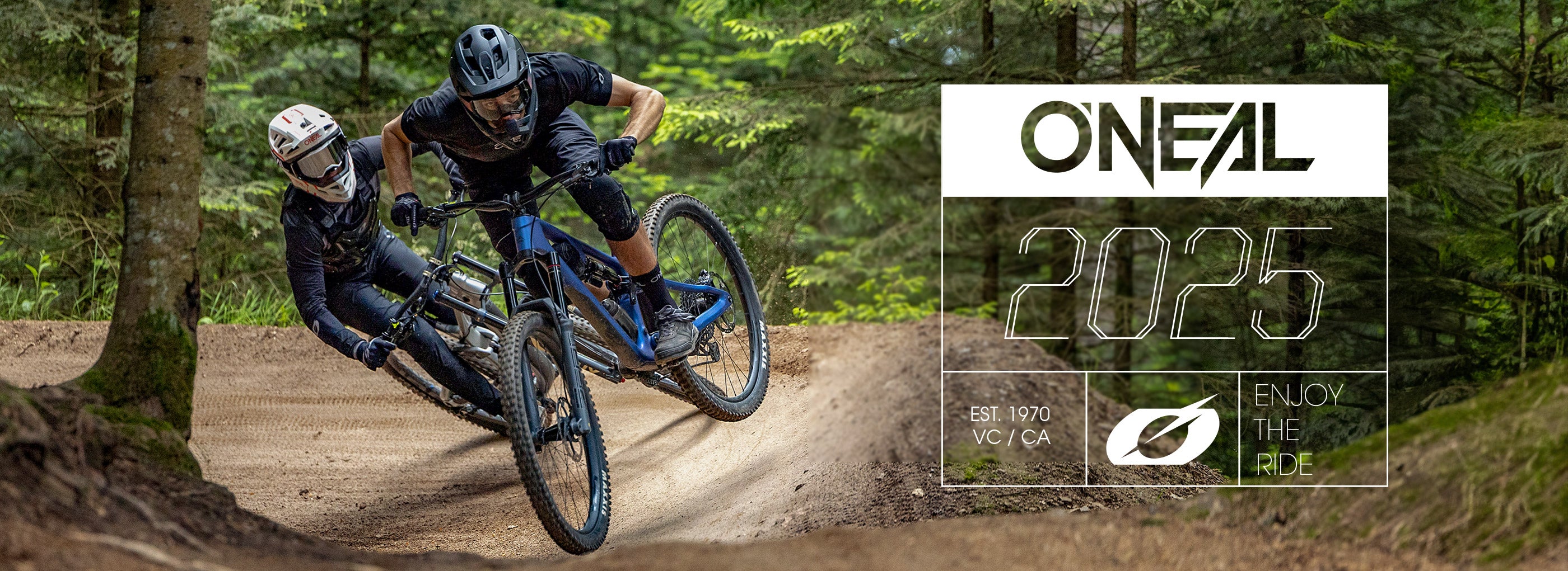 Zwei Radfahrer in voller Montur fahren mit Mountainbikes eine unbefestigte Kurve im Wald. Das Bild zeigt die Texte „ONEAL 2025“ und „ENJOY THE RIDE“ und wirbt damit für die neue Kollektion der Fahrradmarke.