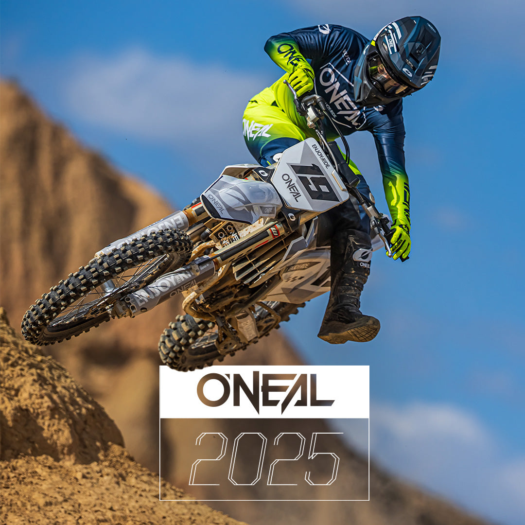Ein Motocross-Fahrer in O'Neal-Ausrüstung springt mit seinem Dirtbike über einen sandigen Hügel, im Hintergrund Berge und blauer Himmel. Am unteren Bildrand ist der Text „ONEAL 2025“ zu sehen.