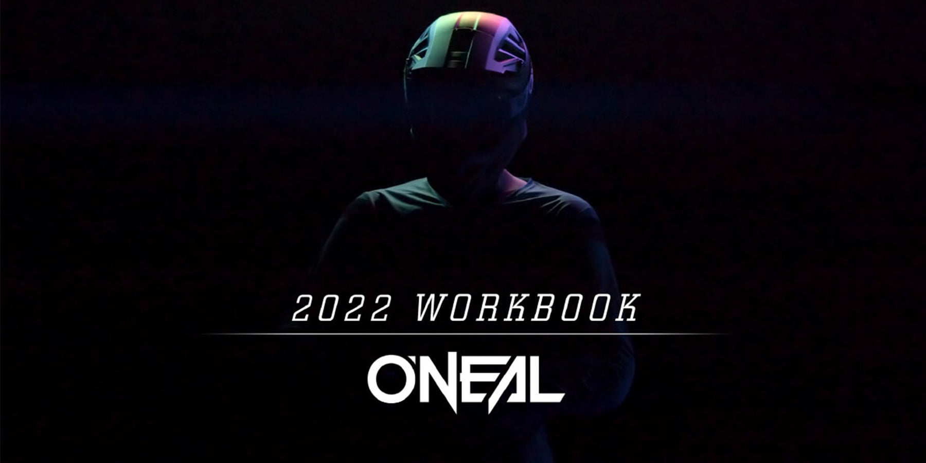 Eine Person in schwarzem Outfit und Helm steht vor einem dunklen Hintergrund. Licht wirft eine Schattensilhouette. Der Text im Vordergrund lautet „2022 Workbook“ mit dem „ONEAL“-Logo darunter.